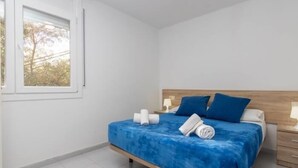 Een slaapkamer met een bed, kussens, een nachtkastje en een raam.