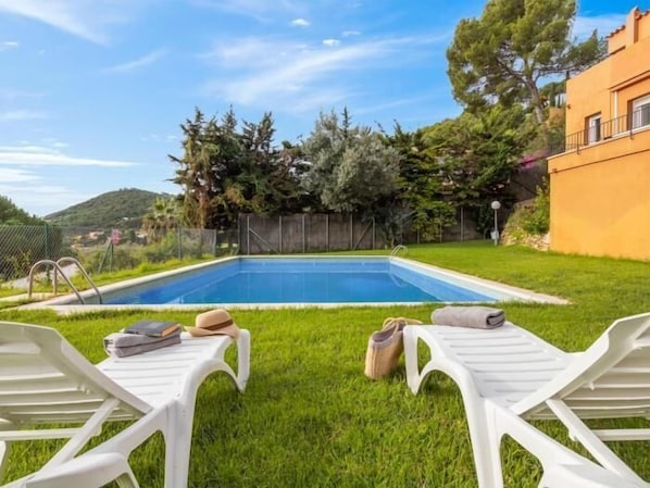 A swimming pool with two white lounge chairs and towels on the grass.