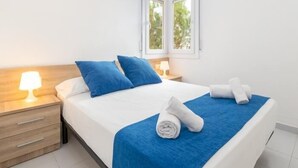 Un lit bien fait, avec une literie bleue et blanche, un plaid bleu et deux serviettes enroulées posées sur le lit.