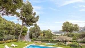 Une piscine rectangulaire à l’eau d’un bleu limpide, entourée d’une pelouse bien entretenue et de quelques chaises longues blanches.