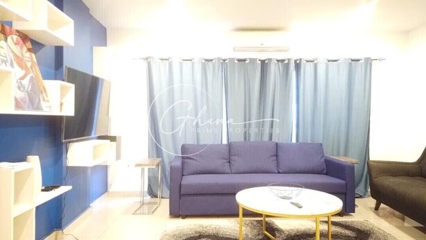 A living room with a blue sofa, a round coffee table, and a TV on a stand. - Luxury 2 Bedroom- The Gallery A32 (Accra)
