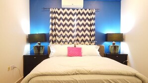 A bedroom with a bed, two bedside tables, a wall-mounted air conditioner, and a patterned curtain. - Luxury 2 Bedroom- The Gallery A32 (Accra)