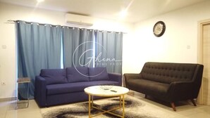 A living room with a blue sofa, a dark armchair, and a small round coffee table. - Luxury 2 Bedroom- The Gallery A32 (Accra)