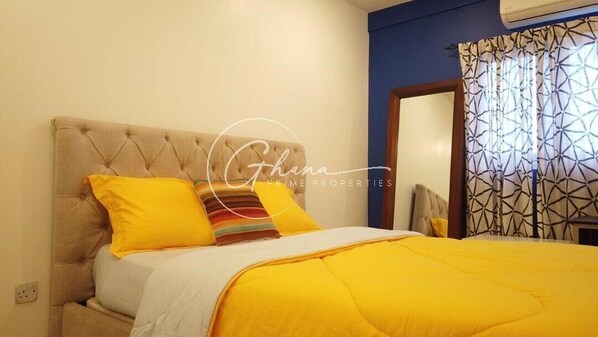 A bedroom with a tufted headboard, a bed with yellow bedding, and a patterned curtain.