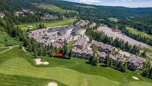 An aerial view of a resort with multiple buildings, a golf course, and surrounding forested hills. - Outdoor Adventure at Sun Peaks 33 (Sun Peaks)