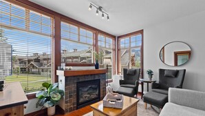A modern living room with a fireplace, large windows, a round mirror, and a grey sofa. - Outdoor Adventure at Sun Peaks 33 (Sun Peaks)