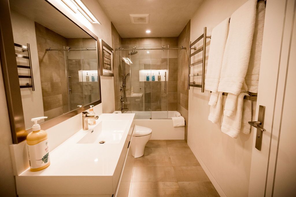 Une salle de bain moderne avec un grand miroir, un lavabo blanc, une douche à parois de verre et des toilettes.