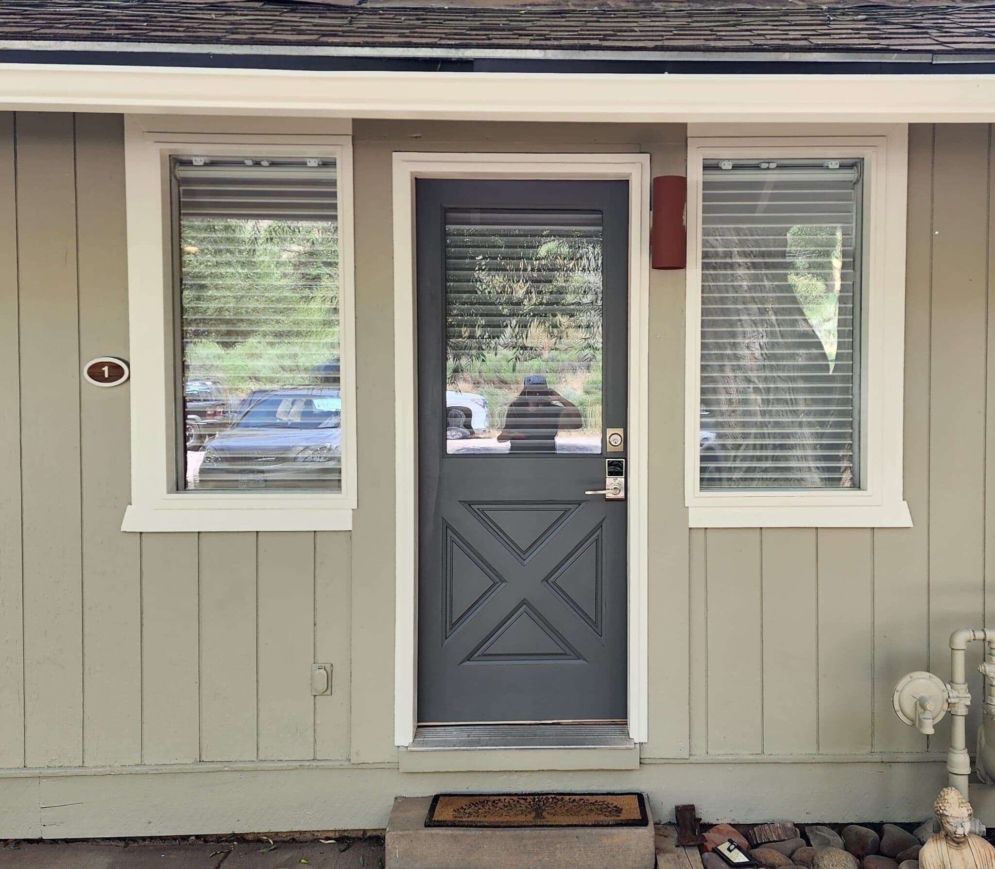 Una casa con puerta gris, dos ventanas con persianas y un buzón pequeño.