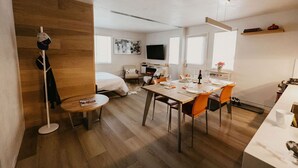 Zona d'estar i menjador oberta i moderna, amb terres de fusta, taula de dinar preparada per a quatre persones i un televisor de pantalla plana penjat a la paret.