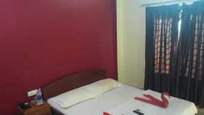 Un letto singolo con biancheria bianca, un comodino in legno con una bottiglia d'acqua e un telefono cellulare sul letto.