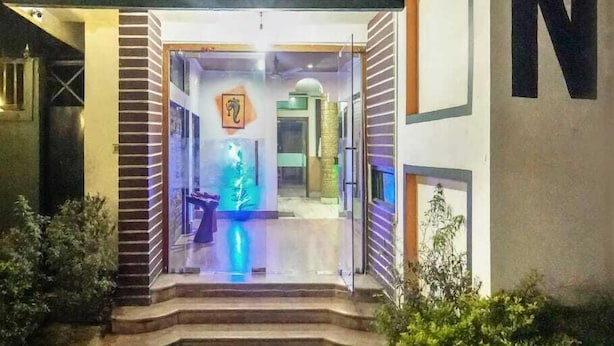 Ingresso di un hotel con una porta in vetro, una piccola piscina illuminata di blu e una scala che conduce verso l'alto.