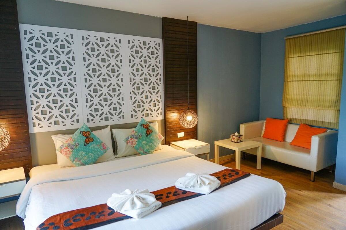 Habitación de hotel con una cama grande, un sofá, un muro decorativo y una ventana con persianas.