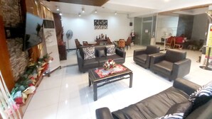 A spacious living room with a large sofa, a coffee table, and a television mounted on the wall. There is a dining area with chairs and a table in the background. - Cosmo Hotel Espana Near Ust (Manila)