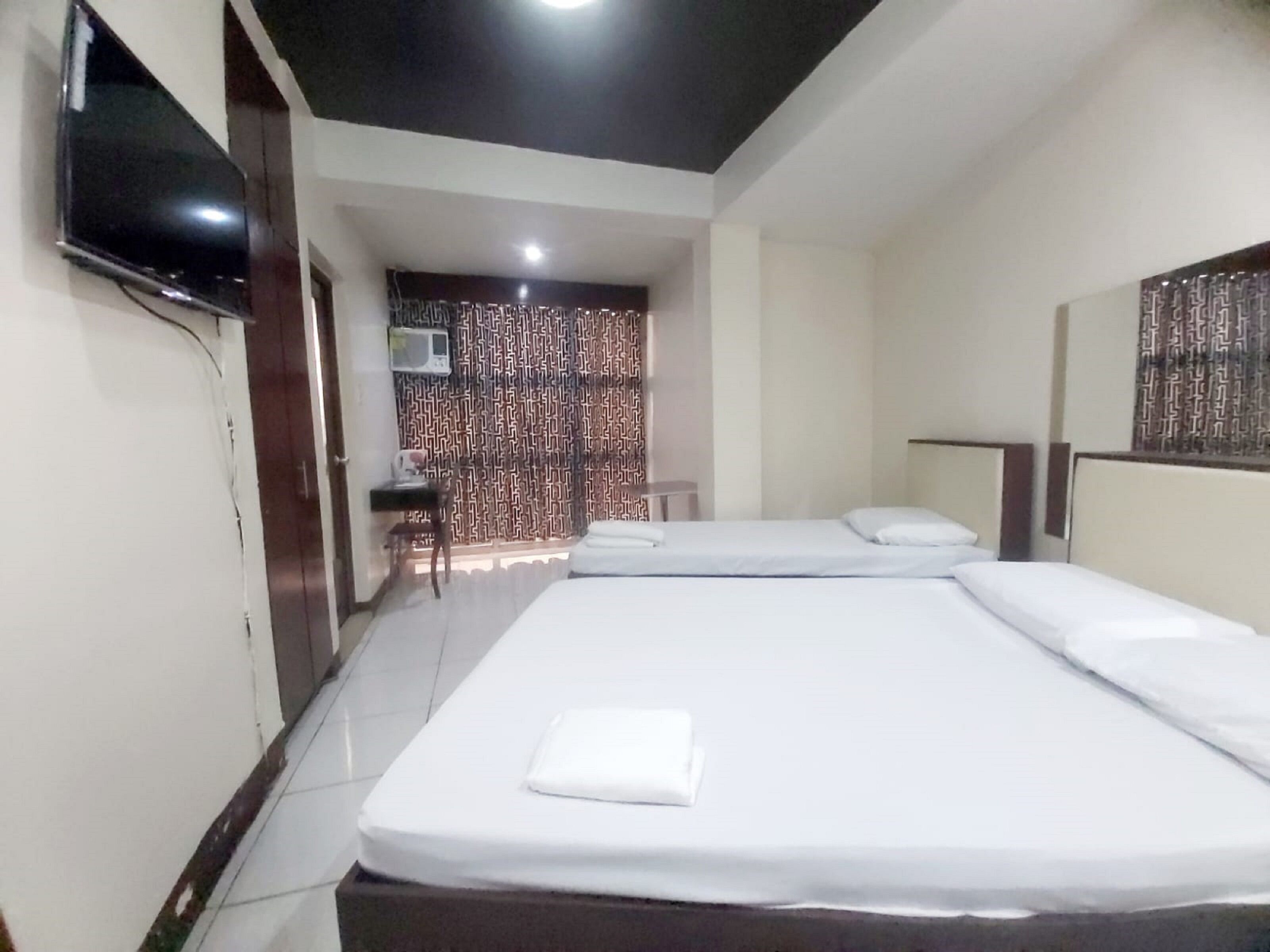 A hotel room with two beds, a TV, a desk with a chair, and a patterned curtain.