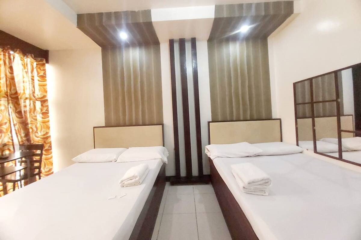 Een hotelkamer met twee eenpersoonsbedden, een stoel, een tafeltje en een spiegel aan de muur.