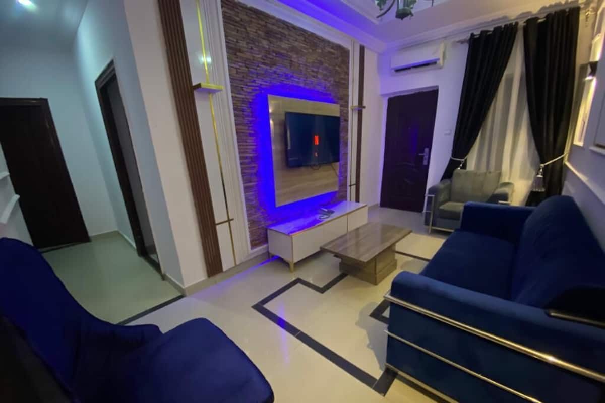 A modern living room with a TV mounted on a brick wall, blue sofas, and a coffee table.