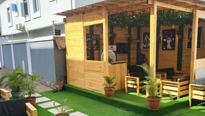 Ein Gartenbereich mit Holzsitzgelegenheiten, Kunstgrasanlage, Pflanzkübeln und einer Barbude.