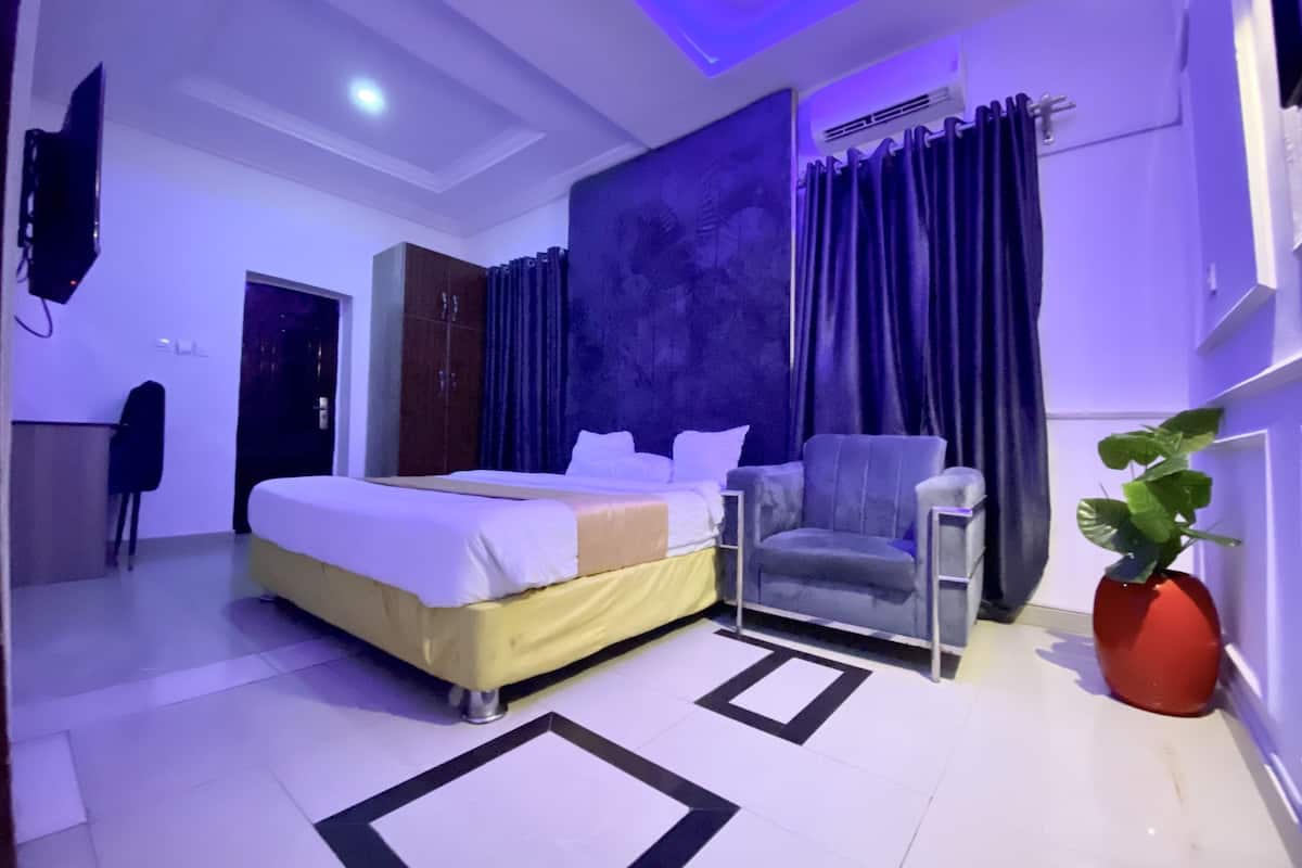 A modern bedroom with a bed, a chair, a small table, and a potted plant.