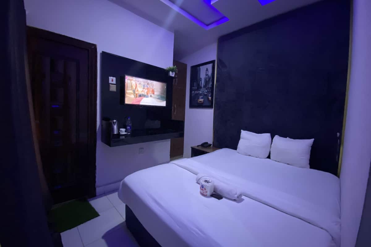 A modern hotel room with a large bed, a flat-screen TV mounted on the wall, a bedside table, and a nightstand.
