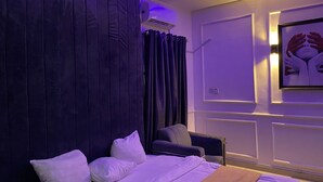 Ein modernes Schlafzimmer mit einem großen Bett, einer dunklen Kopfteil, einem Nachttisch, einem Sessel und einem gerahmten Kunstwerk an der Wand.