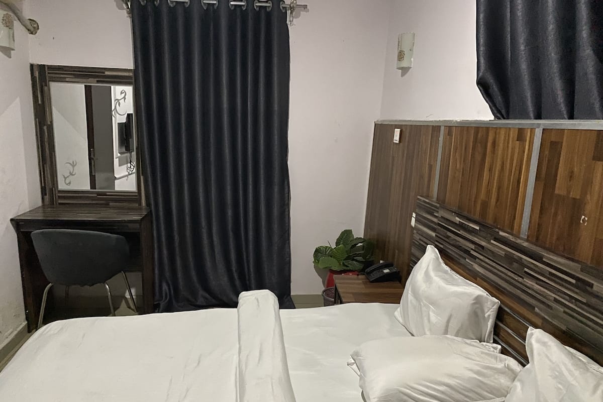 A hotel room with a bed, a desk, a chair, a mirror, and a wardrobe.