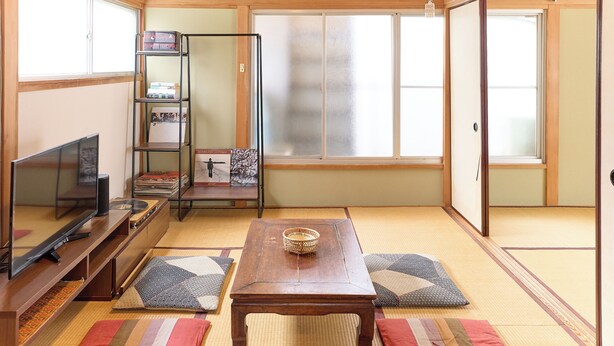 Et traditionelt japansk rum med tatamimåtter, et fjernsyn, et træbord med en skål og en bogreol.