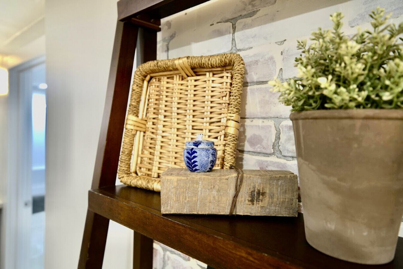 A wicker basket with a blue vase on a wooden shelf against a brick wall.