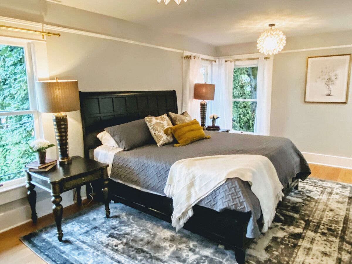 Een slaapkamer met een groot bed, twee nachtkastjes, een wandlamp en een raam met gordijnen.