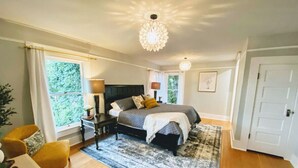 A bedroom with a large bed, a nightstand, a lamp, a chair, and a window with curtains. - A Renovated Historical Home in PNW Monteith District (Albany)