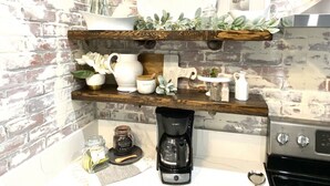 A kitchen with exposed brick walls, wooden shelves, and a coffee maker. - A Renovated Historical Home in PNW Monteith District (Albany)