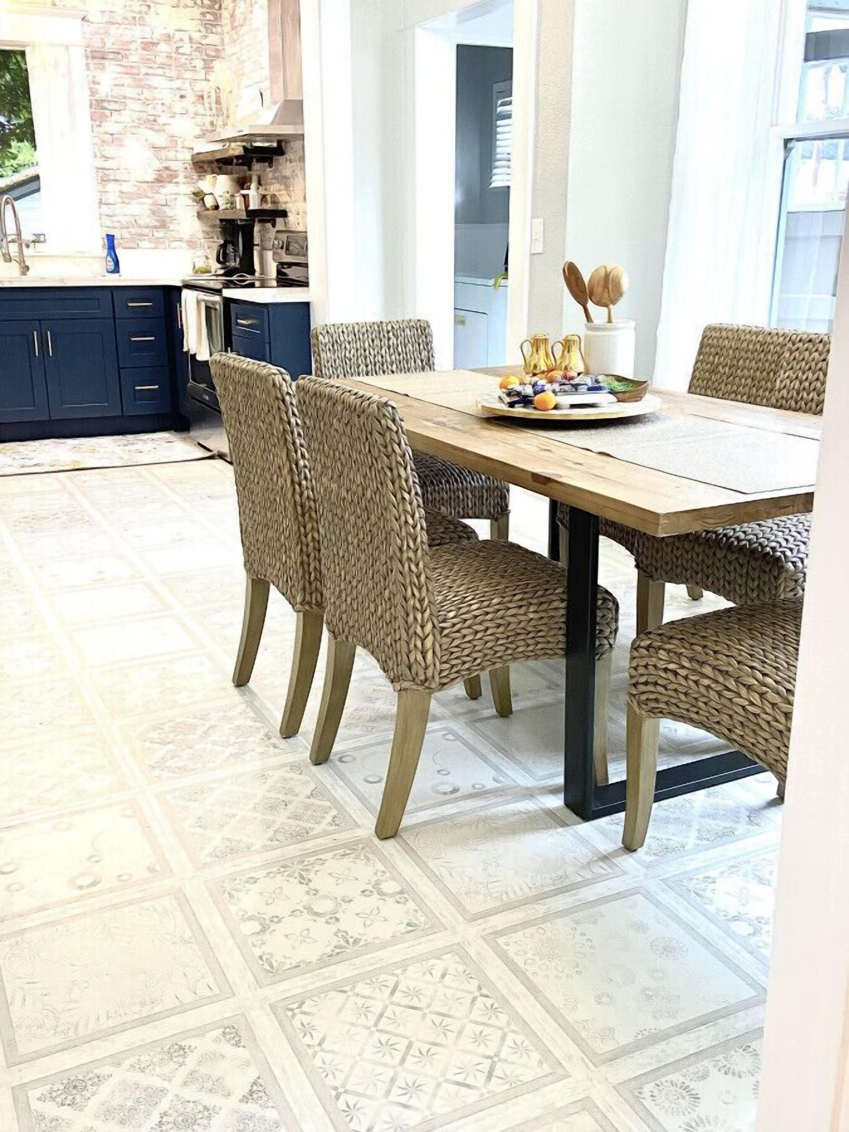 Un coin repas avec une table en bois et des chaises en osier, une cuisine en arrière-plan et des carreaux de sol à motifs.