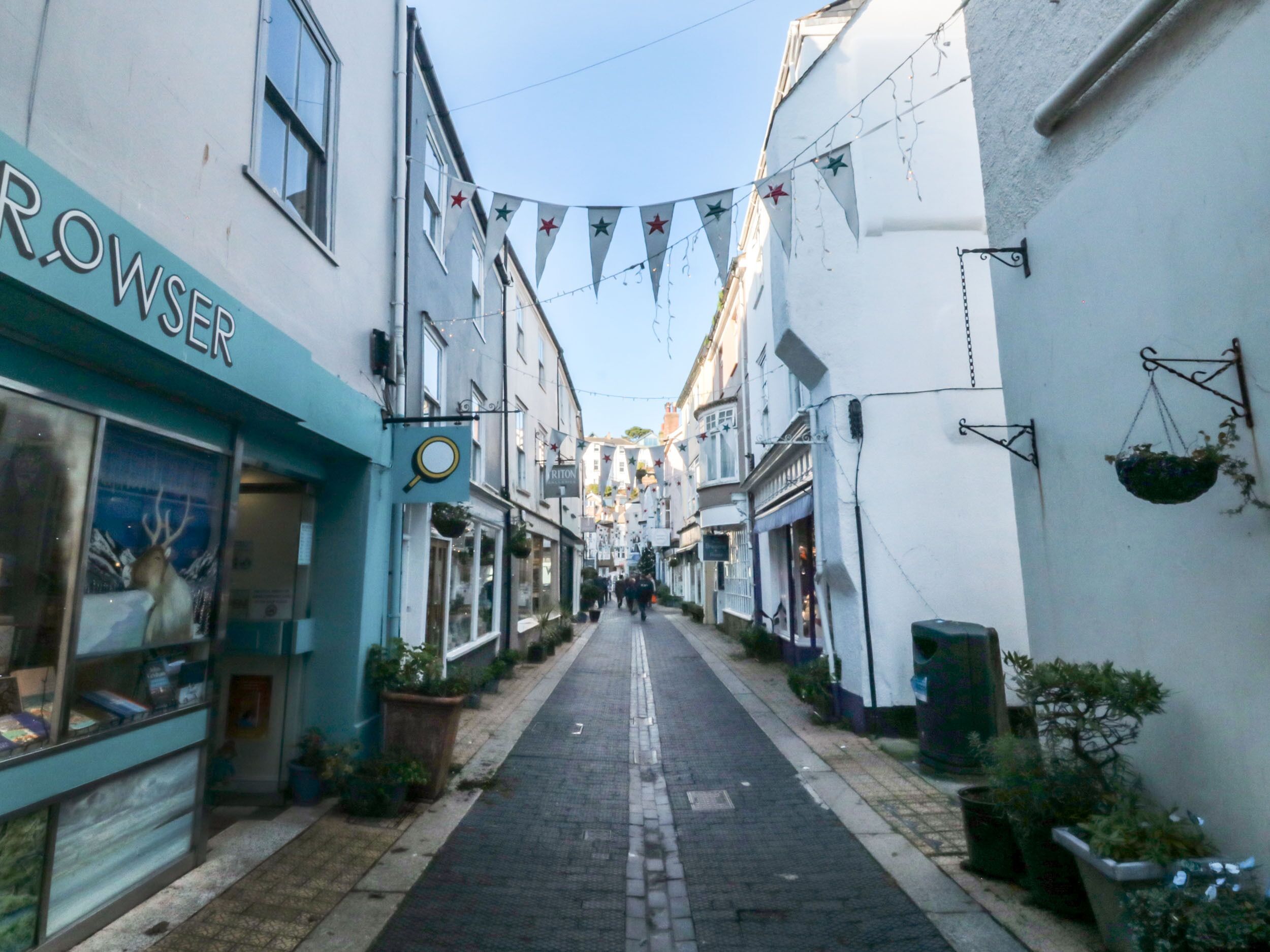 Une rue étroite bordée de boutiques et d’immeubles, avec une enseigne indiquant « ROWSEER », visible sur le côté gauche.