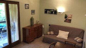 A living room with a brown sofa, a wooden table, and a cabinet. There is a door leading to an outdoor area. - Ground floor in villa (L'Île-Rousse)