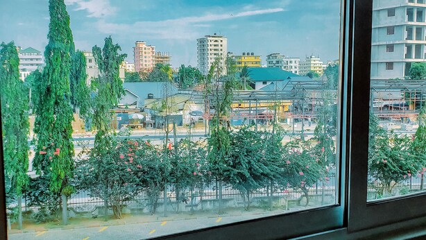 A view through a window of a cityscape with buildings, trees, and a clear sky. - Royal Village Hotel Dar Es Salaam (Dar es Salaam)