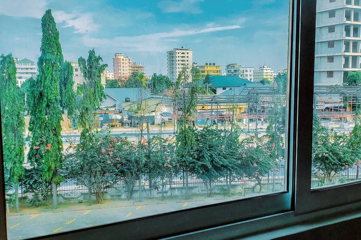 A view through a window of a cityscape with buildings, trees, and a clear sky.