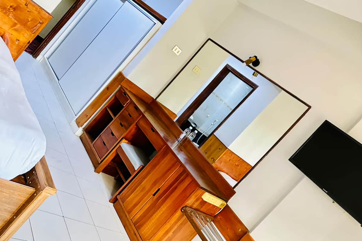 A hotel room with a wooden vanity, a mirror, a flat-screen TV, and a bed.