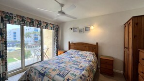 Un dormitorio con cama, ventilador de techo, armario de madera y ventana con cortinas.