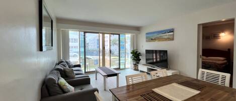 A modern living room with a sofa, a wooden dining table, and a television.