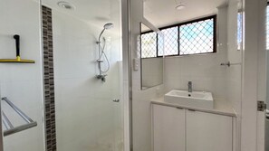 Un baño moderno con ducha, lavabo y ventana con celosía metálica.