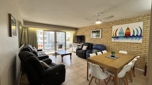 A living room with a sofa set, a dining table with chairs, a TV, and a painting on the wall.