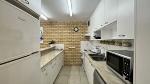 A compact kitchen with white cabinets, a brick backsplash, a clock, and basic appliances. - Dulkara 11 Ocean Breezes and Beachfront Cafes Nearby (Kings Beach)