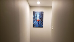 Un pasillo con un cuadro que muestra una callejuela urbana bajo la lluvia y una persona con paraguas.