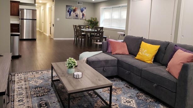 Una sala moderna con un sofá seccional gris, una mesa de centro de madera y una alfombra estampada.