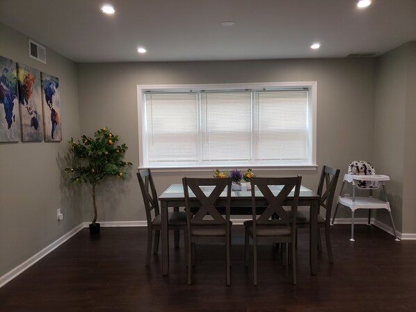 A dining area with a table and chairs, a window with blinds, a potted plant, and artwork on the wall.