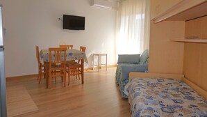 Een kamer met een bed, een aan de muur bevestigde televisie, een eettafel met stoelen en een klein bijzettafeltje.