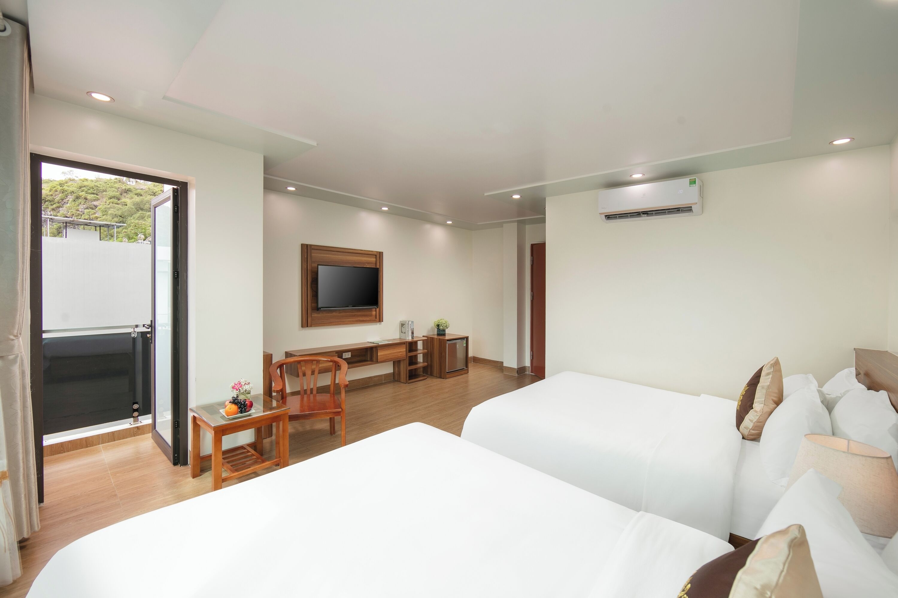 A hotel room with two beds, a desk, a chair, a television, and an air conditioning unit.