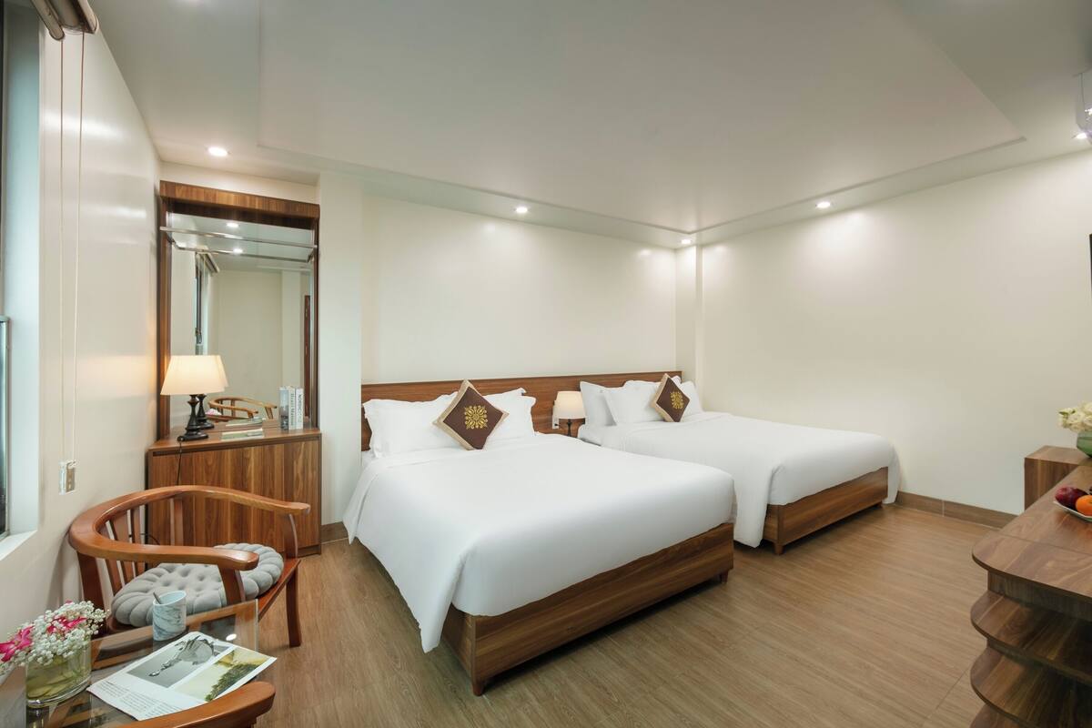 A hotel room with two beds, a wooden chair, a desk with a lamp, and a mirror.