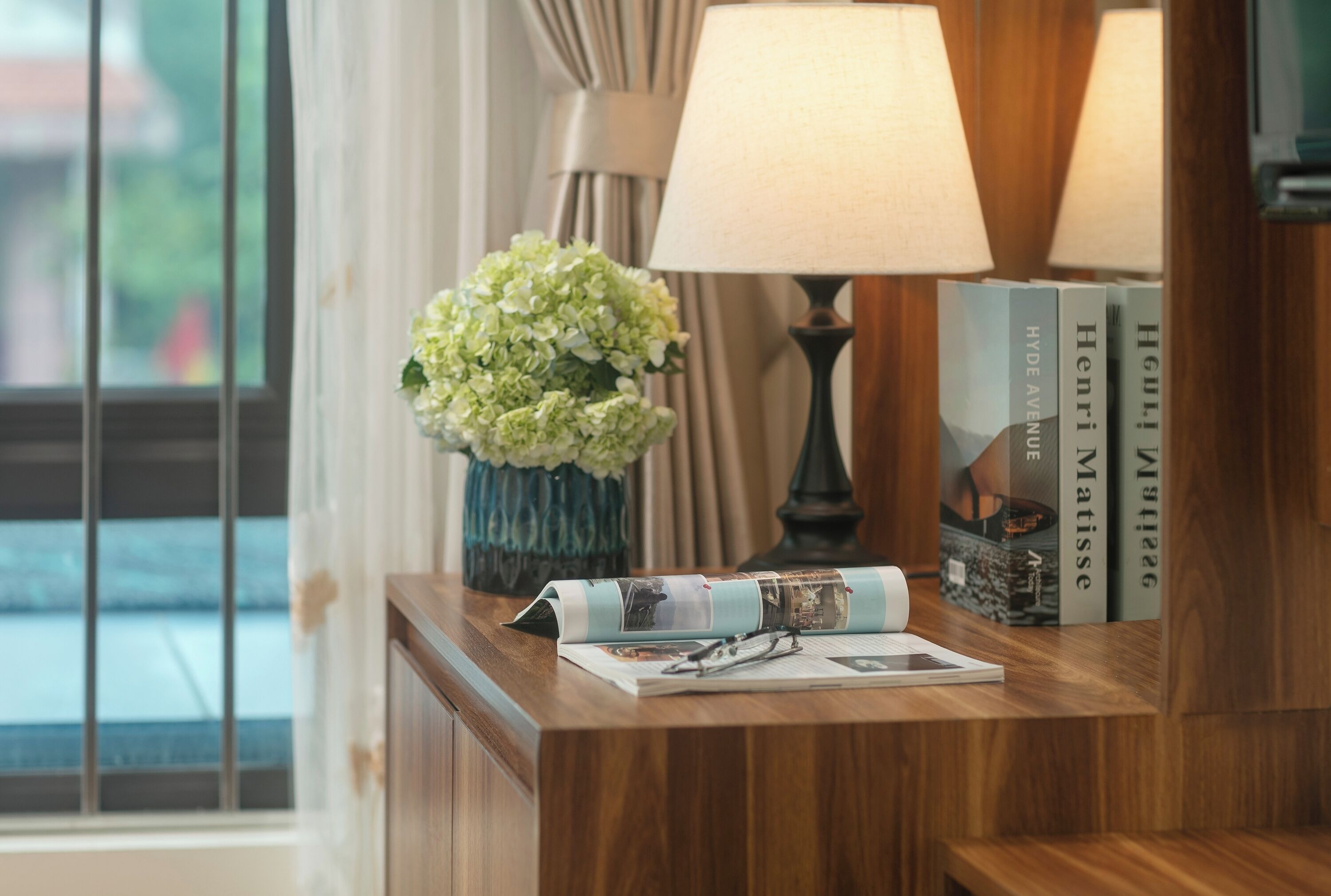 A wooden desk with a lamp, a vase of flowers, and books.