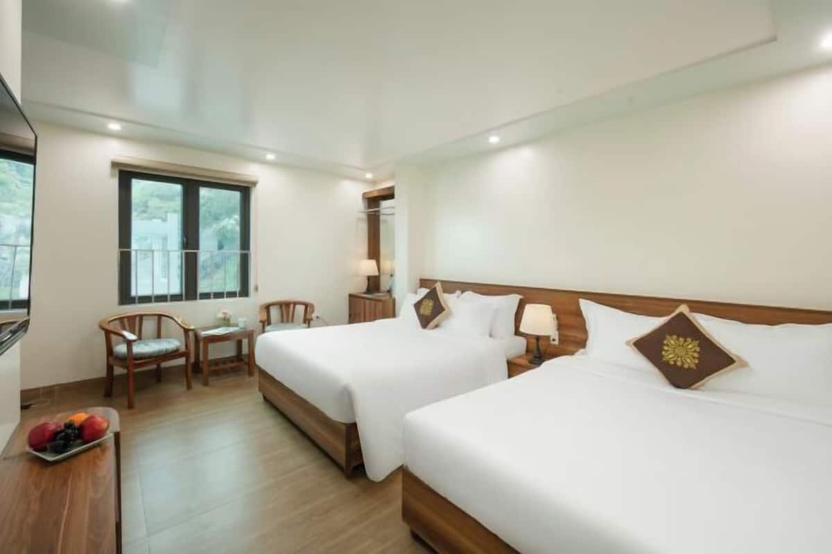 A hotel room with two beds, a small table with fruit, a chair, and a window.