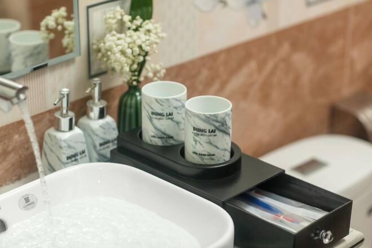 A bathroom with a white sink, two marble-patterned cups on a tray, a mirror, and toiletries.
